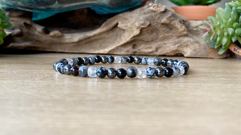 May include: A bracelet made of black, gray, and white beads. The beads are round and have a smooth finish. The bracelet is on a wooden surface.