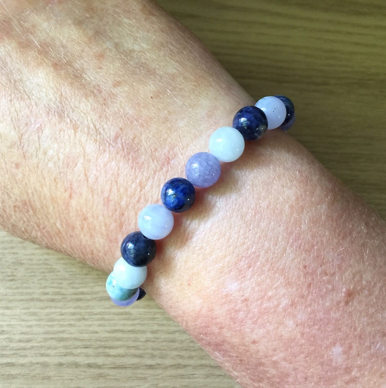 May include: A bracelet made of blue, light blue, and lavender coloured beads. The beads are round and smooth.