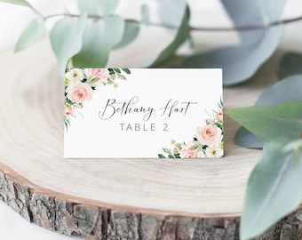 May include: A white place card with pink and white floral accents. The text on the card reads "Bethany Hart TABLE 2".