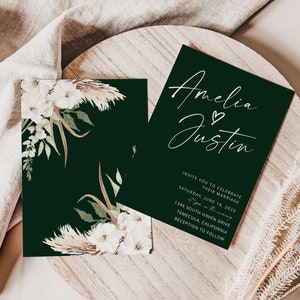 Puede incluir: Una invitaci&oacute;n de boda verde oscuro con caligraf&iacute;a blanca que dice "Amelia & Justin". La invitaci&oacute;n incluye la fecha, la hora y el lugar de la ceremonia y la recepci&oacute;n de la boda. La invitaci&oacute;n est&aacute; decorada con flores blancas y hierba de la pampa.