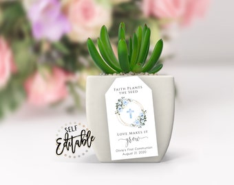 Puede incluir: Una maceta blanca para suculentas con una etiqueta que dice "La fe planta la semilla, el amor la hace crecer." La etiqueta también incluye una cruz, flores azules y el texto "La Primera Comunión de Olivia 21 de agosto de 2020".