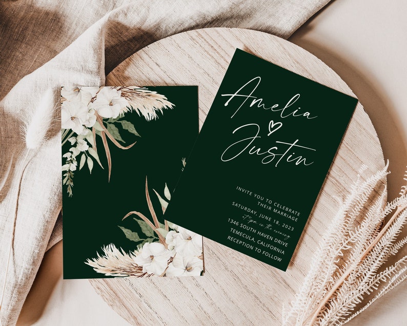 Puede incluir: Una invitaci&oacute;n de boda verde oscuro con caligraf&iacute;a blanca que dice "Amelia & Justin". La invitaci&oacute;n incluye la fecha, la hora y el lugar de la ceremonia y la recepci&oacute;n de la boda. La invitaci&oacute;n est&aacute; decorada con flores blancas y hierba de la pampa.