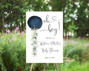 Puede incluir: Un letrero blanco sobre un caballete con el texto "oh boy!" en escritura negra. Un círculo azul marino con vegetación y las palabras "Bienvenida a la fiesta de bienvenida al bebé de Kristina + Matt" también están en el letrero. La fecha "8 de junio de 2021" está en la parte inferior.