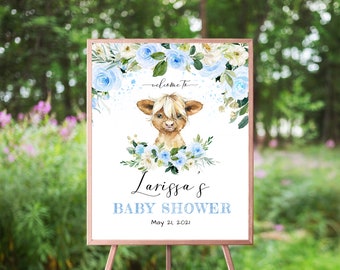 May include: A white baby shower welcome sign with blue and white flowers, a cute brown and white highland cow, and the text "Welcome to Larissa's Baby Shower May 21, 2021".