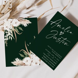 Puede incluir: Una invitaci&oacute;n de boda verde con caligraf&iacute;a blanca que dice "Amelia & Justin" y detalles para la ceremonia y la recepci&oacute;n de la boda. La invitaci&oacute;n est&aacute; decorada con un dise&ntilde;o floral con flores blancas y hierba de la pampa.