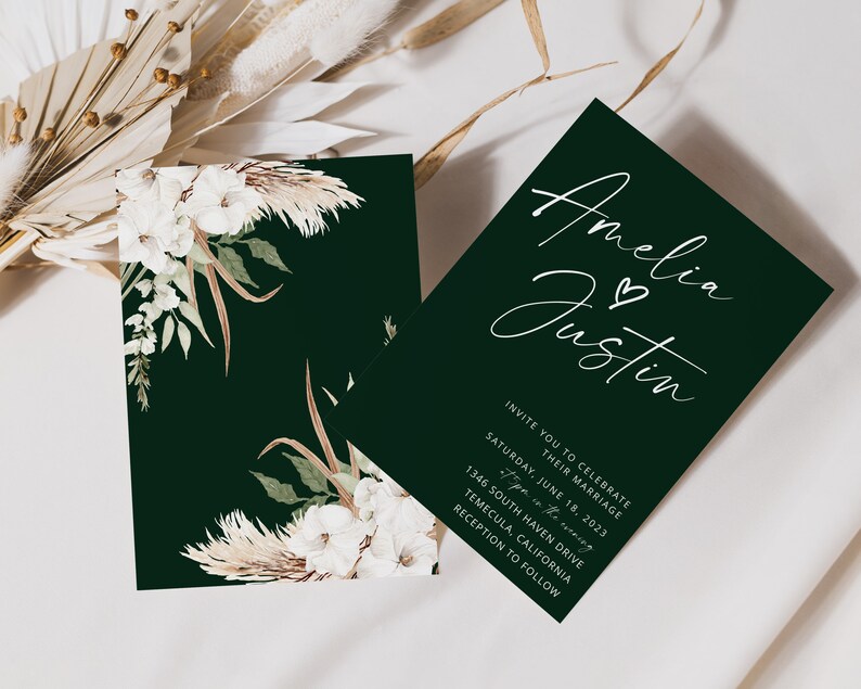 Puede incluir: Una invitaci&oacute;n de boda verde con caligraf&iacute;a blanca que dice "Amelia & Justin" y detalles para la ceremonia y la recepci&oacute;n de la boda. La invitaci&oacute;n est&aacute; decorada con un dise&ntilde;o floral con flores blancas y hierba de la pampa.