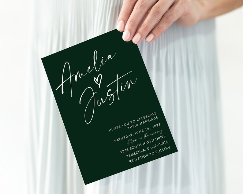Puede incluir: Una tarjeta de invitaci&oacute;n de boda verde oscuro con caligraf&iacute;a blanca que dice "Amelia & Justin" con un peque&ntilde;o s&iacute;mbolo de coraz&oacute;n entre los nombres. La invitaci&oacute;n detalla la fecha, la hora, el lugar y la informaci&oacute;n de la recepci&oacute;n de la boda.