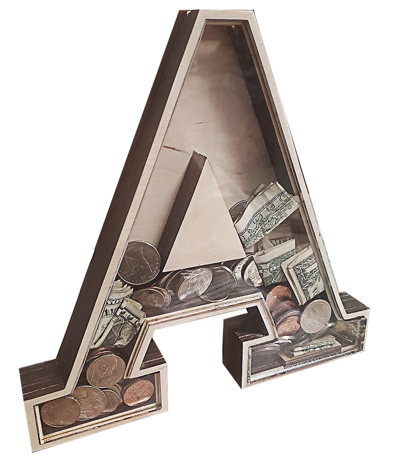May include: A wooden letter A piggy bank with a clear acrylic front. The bank is filled with coins and dollar bills.