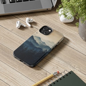 May include: A phone case with a blue and beige design featuring a mountain range with a misty background. The case has a cutout for the phone's camera.
