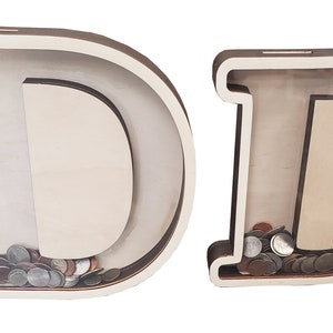 May include: Two wooden piggy banks shaped like the letter D. The piggy banks are made of light brown wood and have a clear plastic front. The piggy bank on the left is empty, while the piggy bank on the right is filled with coins.