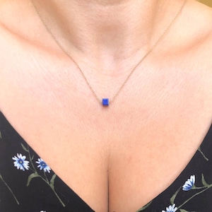 Peut inclure: Un collier délicat en chaîne dorée avec un petit pendentif carré en pierre bleue.
