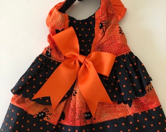 May include: A black and orange Halloween-themed dog dress with a large orange bow, spider web and spider print, and black polka dots.