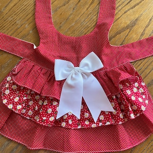 May include: Red and white polka dot dog dress with a white bow and a white daisy print on the bottom ruffle.