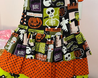 May include: A Halloween-themed pet dress with multiple layers. The top layer is black with Halloween-themed graphics and the word "BOO!". The middle layer is orange with black polka dots, and the bottom layer is green with black cat silhouettes.