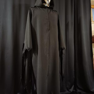 May include: A black hooded robe with jagged edges and a white Scream mask. The costume is displayed on a wooden stand against a black backdrop. The mask has a distorted, screaming expression.