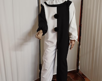 May include: A black and white clown costume on a mannequin. The costume is split down the middle, with one side black and the other white. It has a ruffled collar, black pom-poms, and a hood. The mannequin wears yellow flower-shaped glasses.
