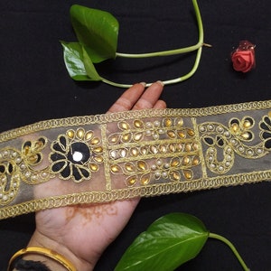May include: Gold and black trim with pearl and mirror embellishments. The trim is on a sheer fabric.