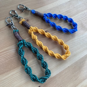 Op de afbeelding: Drie sleutelhangers met bruine lederen accenten en een gedraaid touwontwerp. De sleutelhangers zijn groen, geel en blauw.