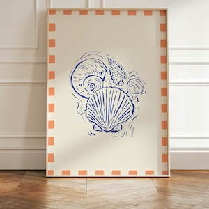 Pode incluir: Uma impressão emoldurada com uma ilustração azul e branca de conchas marinhas sobre um fundo creme. A moldura tem uma borda cor de pêssego com um padrão xadrez.