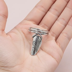Puede incluir: Un anillo de uñas plateado con un diseño floral grabado. El anillo presenta una cubierta de uña curva y alargada y dos bandas que se asientan en el dedo. El diseño incluye un patrón de espiral y puntos. El anillo se muestra en una mano.