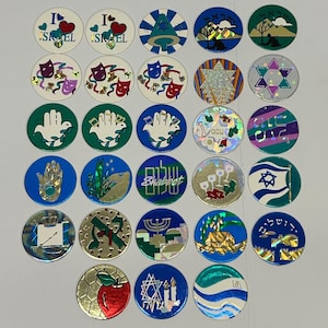 May include: A collection of round, colorful stickers with various designs and text. The stickers feature images of hearts, stars, hands, and other symbols. Some stickers have text in Hebrew and English. The stickers are likely related to Jewish culture and traditions.