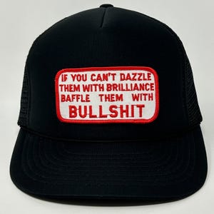 May include: Black trucker hat with a mesh back and a curved brim. The front features a rectangular patch with the text "IF YOU CAN'T DAZZLE THEM WITH BRILLIANCE BAFFLE THEM WITH BULLSHIT" in red letters.