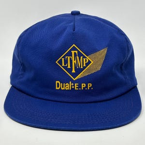 May include: A blue baseball cap with a flat brim. The cap features a yellow and gold logo with the letters "LTMP" inside a diamond shape, and the text "Dual-E.P.P." below the logo.