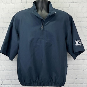 Puede incluir: Una chaqueta de manga corta azul marino con cuello alzado y cremallera parcial. La manga izquierda presenta un logotipo circular blanco con el texto Charity Mega Golf Tournament. La chaqueta tiene un dobladillo recto con banda elástica.