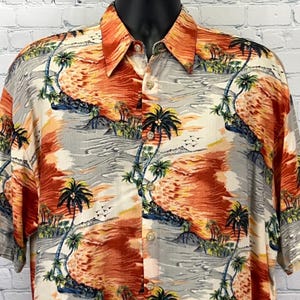 Puede incluir: Camisa de manga corta con un diseño de puesta de sol tropical. La camisa presenta un estampado vibrante de palmeras, olas del océano y una colorida puesta de sol en tonos naranja, rojo y gris. El cuello y los botones son visibles.