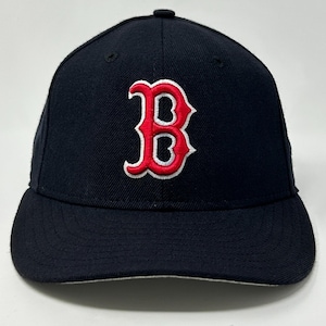 Könnte beinhalten: Marineblaue Baseballkappe mit einem rot-weiß gestickten "B"-Logo. Die Kappe hat einen gebogenen Schirm und eine strukturierte Krone. Das Logo ist ein stilisiertes "B" mit weißer Umrandung.