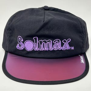 May include: Black cap with a curved, iridescent visor that transitions from purple to pink. The word "Solmax" is embroidered in purple on the front. A small "Solmax" logo is on the visor's edge. The cap has a rounded top.