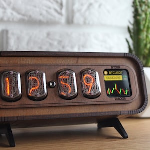 May include: A retro wooden clock showing "12:59" in orange numerals. The clock has a small screen displaying a cryptocurrency chart and the text "BTCUSDT". The clock is on a wooden surface.