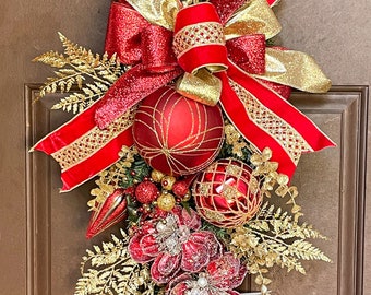 Puede incluir: Una guirnalda de puerta de Navidad roja y dorada con un gran lazo rojo, adornos rojos y dorados y hojas de helecho doradas.
