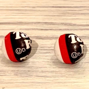 May include: A pair of earrings made from repurposed Tootsie Roll wrappers. The earrings are round and have a black, white, and red color scheme. The Tootsie Roll logo is visible on the earrings.