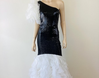 May include: A black sequined, one-shoulder evening gown with a white ruffled accent on the shoulder. The skirt flares out with layers of white ruffles. The dress is displayed on a mannequin.