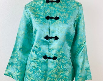May include: A teal blue silk jacket with a black collar and black frog closures. The jacket has a traditional Chinese design with gold embroidery of trees and buildings.