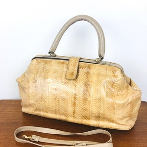 May include: A beige snakeskin handbag with a top handle and a detachable shoulder strap. The bag has a doctor's bag style with a metal clasp closure.