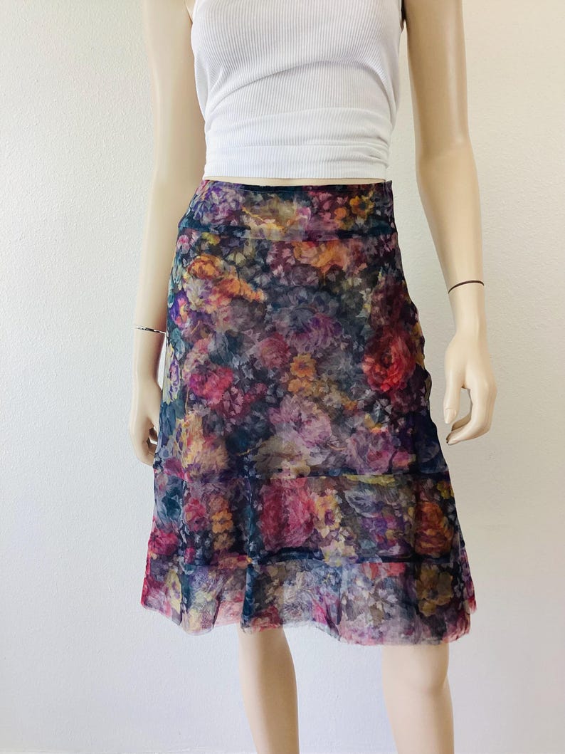 May include: A knee-length skirt with a floral print and tiered hem. The skirt has a dark base with a vibrant floral design in pink, purple, yellow, and orange. The fabric is lightweight and the skirt falls to the knee.