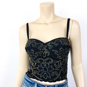 May include: A black and gold embroidered corset top with a sweetheart neckline and adjustable straps. The top has a floral design and is made of a lightweight fabric.