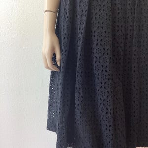 Op de afbeelding: Zwarte eyelet rok met een bloemenpatroon. De rok is geplooid en valt tot halverwege de kuit. De stof heeft een delicaat, openwerk ontwerp, waardoor een textuur ontstaat. De rok wordt op een mannequin getoond.