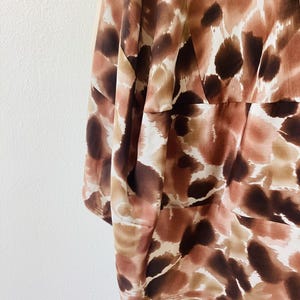 K&ouml;nnte beinhalten: Nahaufnahme eines Kleidungsst&uuml;cks mit einem abstrakten Muster in Braun, Beige und Creme. Der Stoff scheint leicht und flie&szlig;end zu sein, mit einem dezenten Glanz. Das Design weist unregelm&auml;&szlig;ige Formen und Flecken auf.