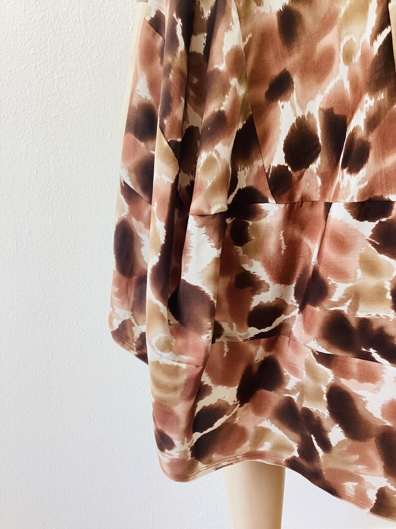 K&ouml;nnte beinhalten: Nahaufnahme eines Kleidungsst&uuml;cks mit einem abstrakten Muster in Braun, Beige und Creme. Der Stoff scheint leicht und flie&szlig;end zu sein, mit einem dezenten Glanz. Das Design weist unregelm&auml;&szlig;ige Formen und Flecken auf.