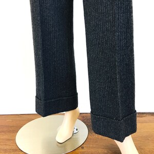 Puede incluir: Un par de pantalones de rayas finas de color gris oscuro con dobladillos. Los pantalones est&aacute;n en un maniqu&iacute; y se ve la parte inferior de los pantalones.