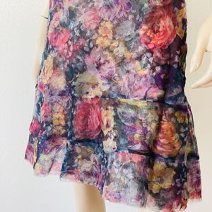 May include: A floral print dress in a vibrant mix of pink, purple, yellow, and orange flowers. The dress has a tiered skirt and a sheer, lightweight fabric. The design is a colourful and feminine style.