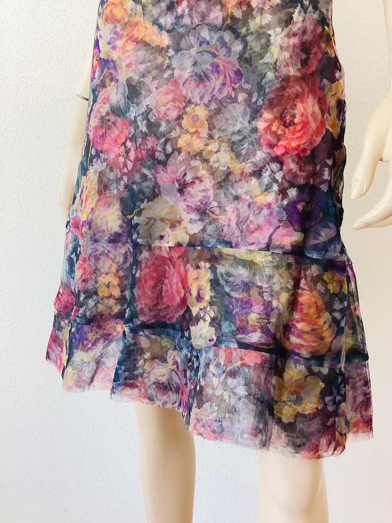 May include: A floral print dress in a vibrant mix of pink, purple, yellow, and orange flowers. The dress has a tiered skirt and a sheer, lightweight fabric. The design is a colourful and feminine style.