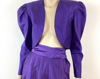 May include: A purple cropped jacket with puffed sleeves and a matching pair of wide-leg pants.