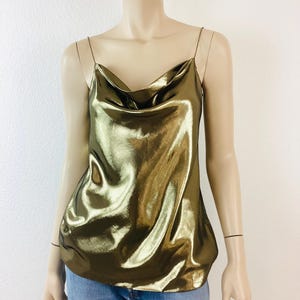 May include: A gold metallic sleeveless top with a cowl neck. The top is made of a silky material and has a relaxed fit.