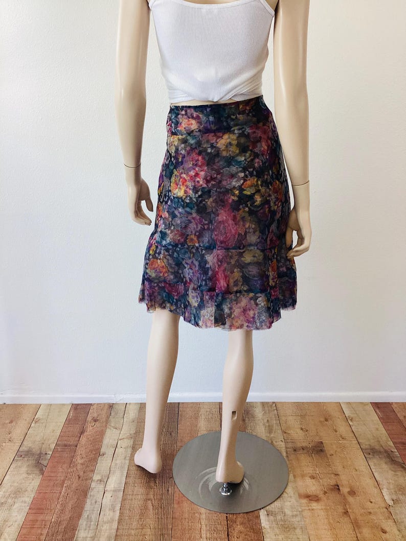 May include: A-line skirt with a floral pattern in shades of purple, pink, and yellow. The skirt has a ruffled hem and is made of a sheer fabric. The mannequin is also wearing a white vest top.
