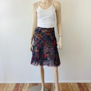 May include: A mannequin wearing a white vest top and a knee-length skirt. The skirt has a colourful floral pattern with shades of blue, purple, and pink. The skirt has a ruffled hemline.