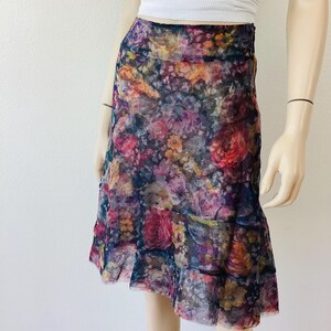 May include: A floral print skirt with a vibrant mix of pink, purple, yellow, and orange flowers on a dark background. The skirt has a layered, ruffled hemline and a flowing silhouette, suitable for a spring or summer outfit.